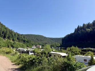 Ein ruhiger See umgeben von grünen Bäumen. Campingfahrzeuge sind am Ufer verteilt.
