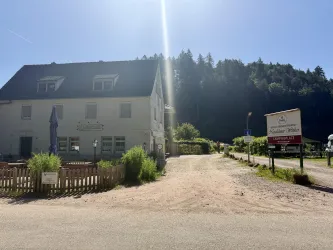 Ein charmantes Gebäude mit einem kleinen Garten und einem Parkplatz. Im Hintergrund sind Bäume und die Natur sichtbar.