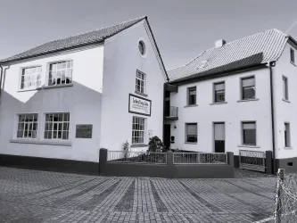 Eine Szene mit zwei weißen Gebäuden, die nebeneinander stehen. Der Platz dazwischen ist gepflastert und bietet einen klaren Blick auf die Architektur.