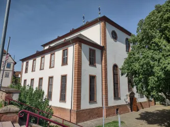 Ein historisches Gebäude mit einer weißen Fassade und großen Fenstern. Umgeben von Bäumen und einem kleinen Garten.