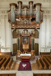 Eine prächtige Kirche mit einer großen Orgel im Hintergrund. Der Altar ist im Mittelpunkt, umgeben von Holzbänken und einem Teppich.
