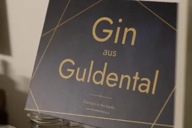 Ein Schild mit der Aufschrift "Gin aus Guldental". Es hat ein modernes Design mit geometrischen Linien.