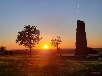 Ein Sonnenuntergang hinter einem großen Stein mit Bäumen im Vordergrund. Die Landschaft ist ruhig und malerisch.