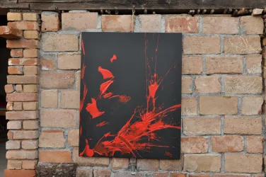 Ein modernes Kunstwerk mit roten Farbklecksen auf schwarzem Hintergrund. Es hängt an einer Ziegelwand.