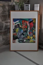 Ein buntes Gemälde mit abstrakten Formen und lebhaften Farben. Der Rahmen ist aus Holz und das Bild steht in einem modernen Raum.