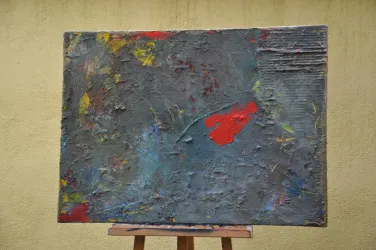 Ein abstraktes Gemälde mit verschiedenen Farben, hauptsächlich Grau, Blau und Rot. Die Struktur ist rau und vielfältig, mit reflektierenden Oberflächen.