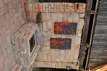 Zwei schwarze Bilder mit rotem Kunstwerk hängen an einer gemauerten Wand. Die Wand besteht aus handgemachten Ziegelsteinen.