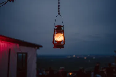 Eine hängende Laterne strahlt warmes Licht in die dunkle Umgebung. Im Hintergrund sind verschwommene Lichter zu sehen.