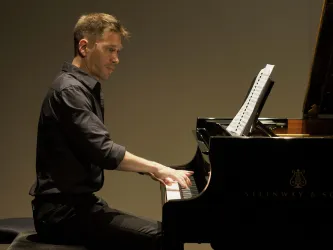 Ein Pianist spielt konzentriert am Klavier. Notenblätter liegen vor ihm auf dem Pult.
