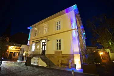 Ein charmantes Gebäude bei Nacht, beleuchtet mit bunten Lichtern. Die Fassade ist gut sichtbar, und es gibt eine einladende Treppe.