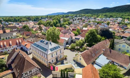 Eine malerische Stadtansicht mit traditionellen Häusern und grünen Bäumen. Die Landschaft ist von sanften Hügeln umgeben.