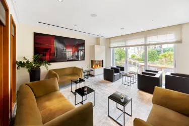 Ein modernes Wohnzimmer mit bequemen Sofas und stilvollen Tischen. Große Fenster bieten Blick auf den Garten und sorgen für viel natürliches Licht.