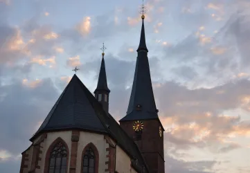Eine Kirche mit hohen Türmen und einem historischen Stil. Der Himmel ist mit sanften Wolken in verschiedenen Farben geschmückt.