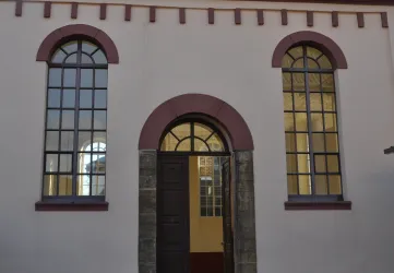 Eine historische Fassade mit großen Fenstern und einer auffälligen Eingangstür. Die Architektur kombiniert moderne und klassische Elemente.