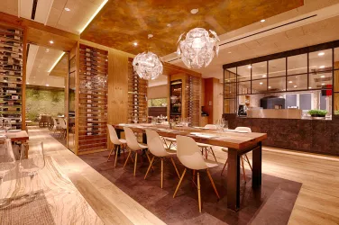 Ein modernes Restaurant mit einem großen Holztisch und eleganten Stühlen. Die Wände sind mit Holz und Glas gestaltet, sanftes Licht schafft eine einladende Atmosphäre.