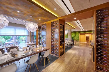 Ein modernes Restaurant mit eleganter Einrichtung und viel natürlichem Licht. Die Holzdecke und der grüne Akzentbereich schaffen eine einladende Atmosphäre.
