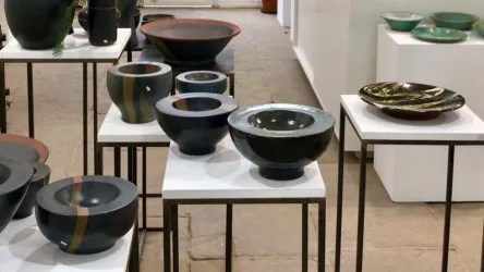 Eine Ausstellung mit verschiedenen keramischen Schalen auf weißen Tischen. Die Schalen zeigen unterschiedliche Farben und Formen.