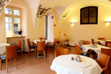 Ein gemütliches Restaurant mit runden Tischen und Holzstühlen. Die Wände sind hell gestrichen und es gibt große Fenster, die viel Licht hereinlassen.