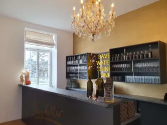 Eine elegante Bar mit einem schönen Kronleuchter und einem gut gefüllten Regal für Gläser. An der Wand steht der Slogan "Save water, drink wine".