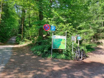 Ein Weg im Wald mit einem Parkplatzschild und einer Karteninformation. Zwei Fahrräder sind neben dem Schild abgestellt.