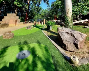 Eine Minigolfanlage mit grünem Kunstrasen und verschiedenen Steinen. Bäume und natürliche Elemente sorgen für eine entspannte Atmosphäre.