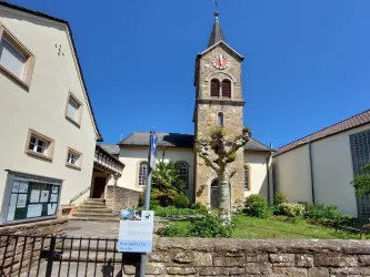 Ein historisches Gebäude mit einem Kirchturm und einem schönen Garten. Der Himmel ist klar und blau.