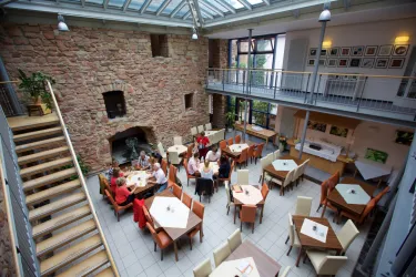 Ein gemütliches Restaurant mit einer offenen Galerie und einem warmen Steinmauerdesign. Tische sind umgeben von Gästen, die zusammen essen und sich unterhalten.