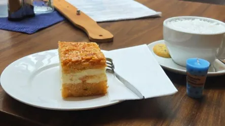 Ein Stück Kuchen auf einem Teller mit einer Gabel daneben. Neben dem Kuchen steht eine Tasse mit Milch und ein kleiner Keks.