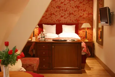 Ein gemütliches Zimmer mit einem Doppelbett und eleganter Holzkommode. Die Wände sind mit hübschem Blumenmuster dekoriert und das Ambiente ist einladend.