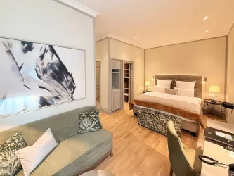 Ein modernes Hotelzimmer mit einem komfortablen Bett und einem gemütlichen Sofa. Es gibt helle Wände und dekorative Elemente, die dem Raum eine elegante Atmosphäre verleihen.