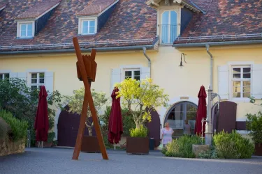 Ein charmantes Gebäude mit gelber Fassade und einem schönen Garten. Im Vordergrund steht eine große Holzskulptur und einige Sonnenschirme.