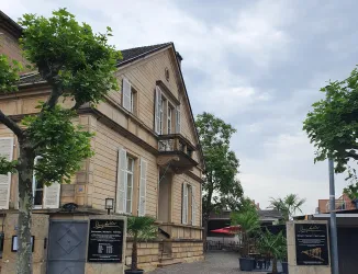 Ein schönes, historisches Gebäude mit einer hellen Fassade. Umgeben von Bäumen und einer einladenden Außenanlage.