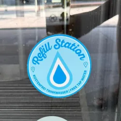 Ein Aufkleber mit der Aufschrift "Refill Station" und einem Wassertropfen. Darunter steht "Kostenfrei Trinkwasser" in deutscher Sprache.