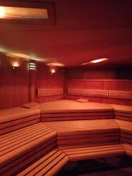 Eine helle Sauna mit holzvertäfelten Bänken und sanfter Beleuchtung. Der Raum vermittelt eine entspannende Atmosphäre.
