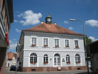 Ein hübsches Gebäude mit einem roten Dach und weißen Fenstern. Der Himmel ist blau mit einigen Wolken.