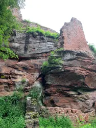 Ruinen einer alten Burg aus rotem Sandstein. Üppiges Grün umgibt die Felsen. Hier sind Teile der Burgruine Breitenstein zu sehen.