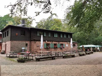Ein rustikales Restaurant im Wald mit einer Holzfassade. Vor dem Gebäude stehen Tische und Bänke im Freien. Zu sehen ist hier das Waldhaus Lambertskreuz. Eine bewirtschaftete Hütte im Pfälzerwald gelegen.