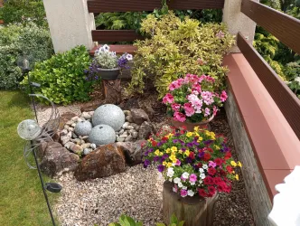 Ein schöner Gartenbereich mit bunten Blumen und grünen Pflanzen. In der Mitte befindet sich eine kleine Steinformation, umgeben von Kieselsteinen.