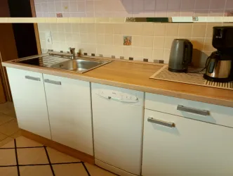 Eine moderne Küche mit Holzarbeitsplatte, Spüle und Elektrogeräten. Die Küchenschränke sind in Weiß gehalten und der Boden hat ein gefliestes Muster.