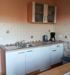 Eine moderne Küche mit einer Spüle, einem Kühlschrank und einer Kaffeemaschine. Die Wände sind hell und die Möbel sind in neutralen Farben gehalten.