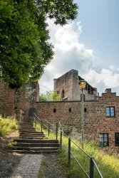 Die Burg Spangenberg erhebt sich malerisch hinter einer alten Steintreppe, umgeben von grünen Bäumen unter einem strahlend blauen Himmel mit sanften Wolken.