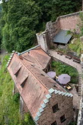 Die Burgschänke Burg Spangenberg mit roten Ziegeldächern und grüner Umgebung. Im Vordergrund sind Tische mit Schirmen zu sehen.