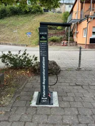 Eine Fahrrad-Reparaturstation steht an einer Straße. Sie ist mit Werkzeugen und einer Luftpumpe ausgestattet.