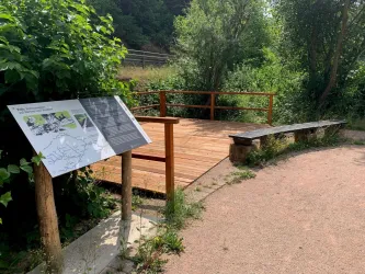 Ein ruhiger Aussichtspunkt mit einer Holzplattform und einer Bank. Umgeben von grüner Vegetation und einem Kiesweg.