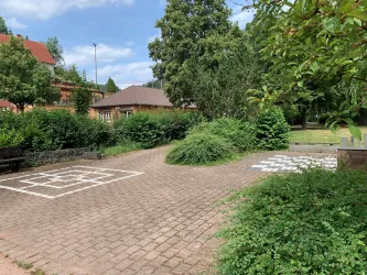 Ein ruhiger Platz mit gepflastertem Boden und viel Grün. Im Hintergrund sind Bäume und ein Spielplatz sichtbar.