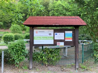Ein Informationsschild in einem grünen Bereich. Das Schild enthält verschiedene Hinweise und Pläne zur Umgebung.