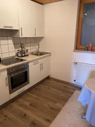 Eine moderne Küche mit weißen Schränken und einem Kochfeld. Der Boden ist mit Holzdielen ausgelegt und es gibt ein Fenster, das natürliches Licht hereinlässt.