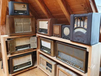 Eine Sammlung alter Radiogeräte in einem Holzregal. Die Radios haben verschiedene Designs und sind in warmen Farben gehalten.