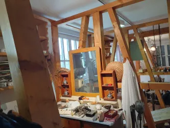Ein kreatives Atelier mit Holzrahmen und einem großen Spiegel. Verschiedene Werkzeuge und Materialien sind auf einem Tisch verteilt.