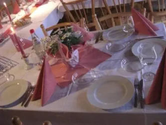 Ein schön dekorierter Tisch mit weißen Tellern und roten Servietten. Kerzen und Blumenarrangements schaffen eine einladende Atmosphäre.